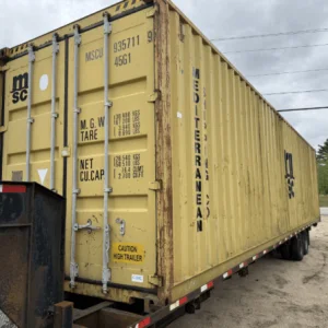 Yellow used 40ft container carried on a trailer beside a rural road