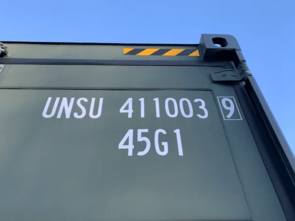 Top corner of a green container against blue sky, stencilled with its owner code and type code