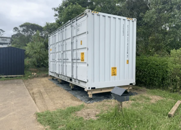 White 20ft open side container on grass, seen from the corner on a cloudy day