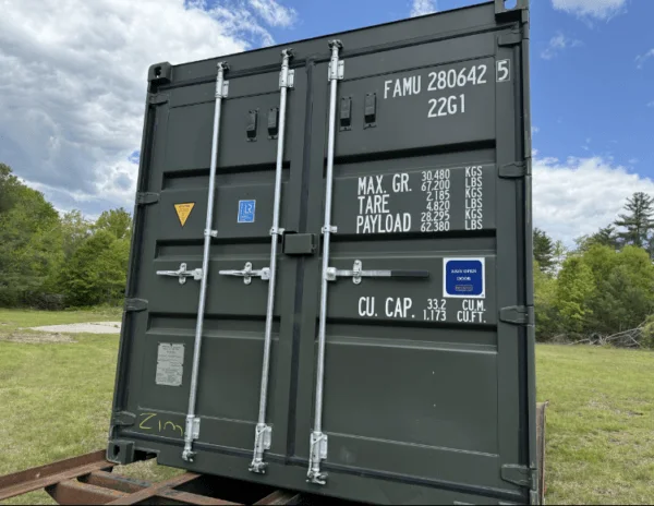 Cargo doors and data panel on a green 20ft container resting on a trailer in a field