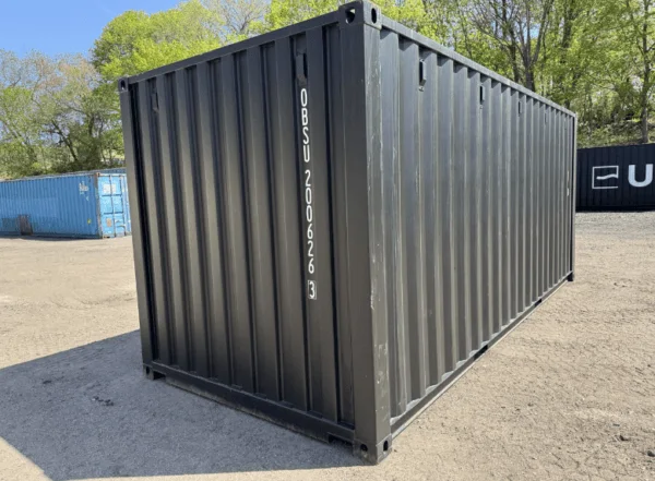 Matte black 20ft container seen from the corner on gravel, with trees behind