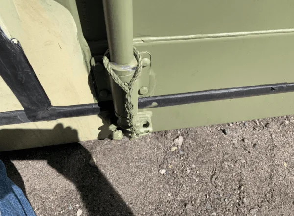 Bottom corner fitting and side rail of a camouflage painted container on gravel