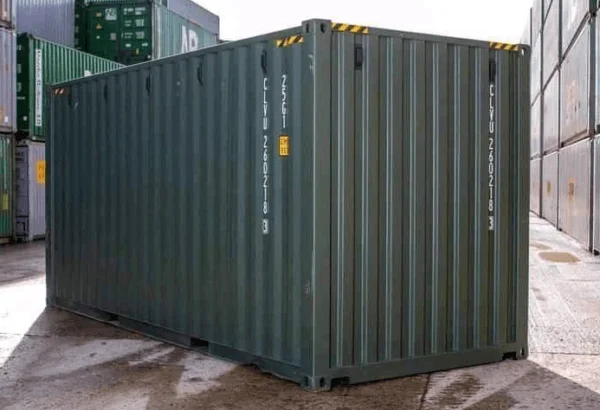 Rear corner of a green 20ft container standing on a wet concrete yard
