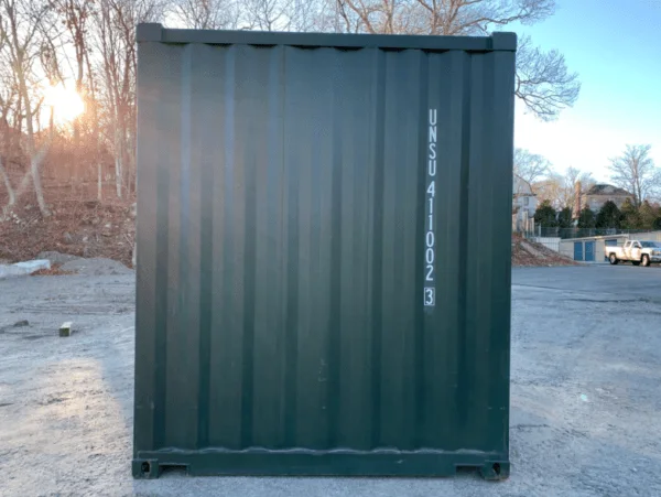Side elevation of a green 10ft container backlit by the sun, with bare trees behind