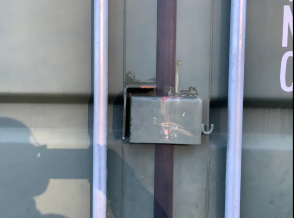 Close-up of the welded steel lockbox protecting the padlock on the container doors