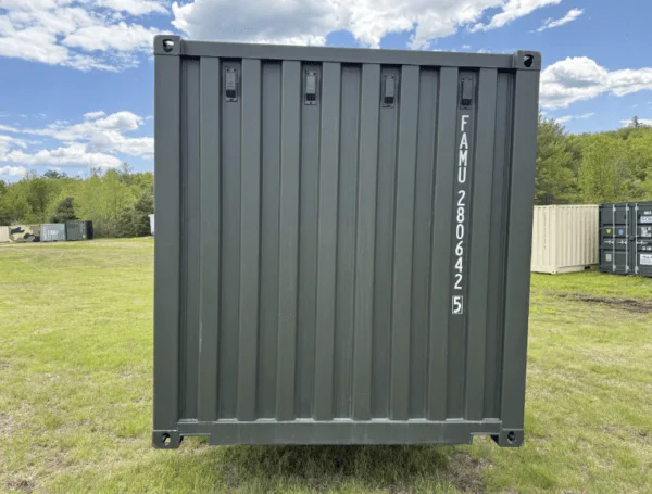 End wall of a green 20ft container standing in a grassy field under a blue sky