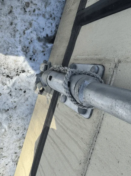Locking bar bracket bolted to a beige container door above snowy ground