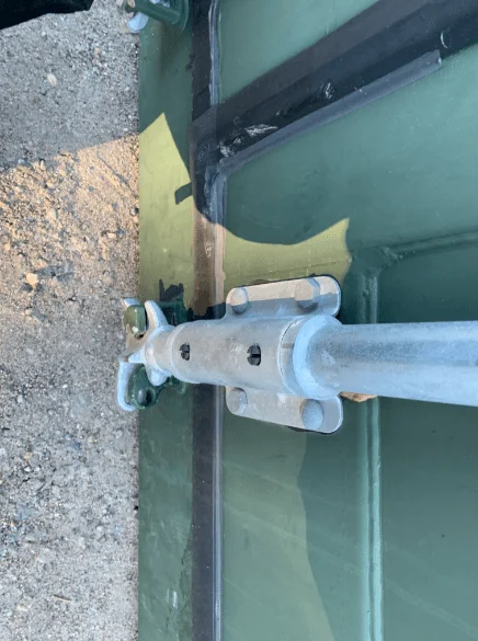 Galvanised cam keeper securing a locking bar against the green container door