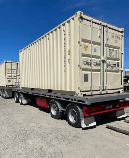 Beige one trip 20ft container secured on a flatbed trailer at a depot