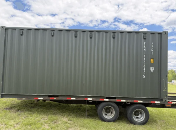 Green 20ft container carried on a twin axle trailer across an open field