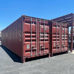 Two dark red open side containers standing side by side in a yard