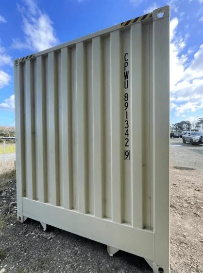 End wall of a beige 40ft container standing on gravel under a blue sky