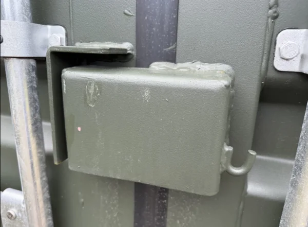 Painted steel lockbox welded over the door handles of a green 20ft container