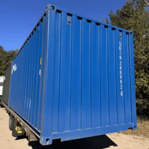 Blue 20ft container loaded on a trailer with pine trees in the background