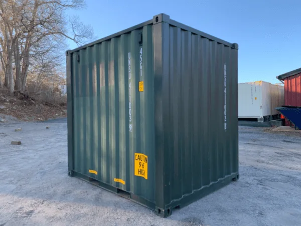 Green 10ft container standing on a gravel yard, seen from the corner in low winter sun