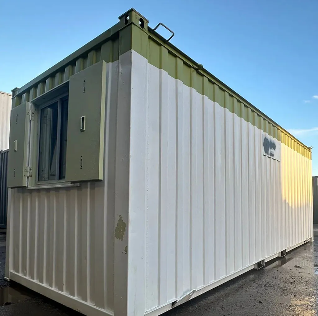 Green and white container office cabin with a shuttered window, seen from the corner