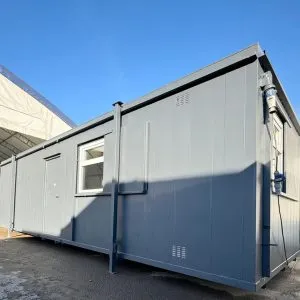 Long grey and white portable cabin with windows, standing on adjustable legs