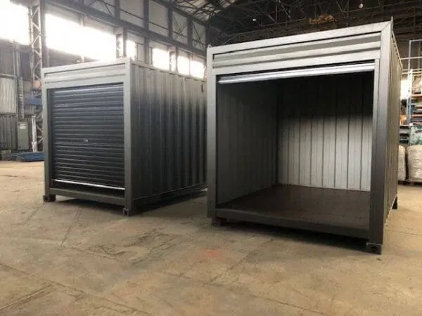 Two roller shutter storage containers inside a warehouse, one shutter open on an empty interior