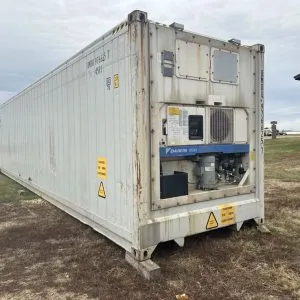 White reefer container standing on rough grass with its chiller unit exposed