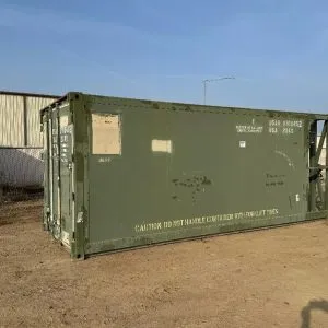 Olive drab military container standing on sand, seen along its side wall